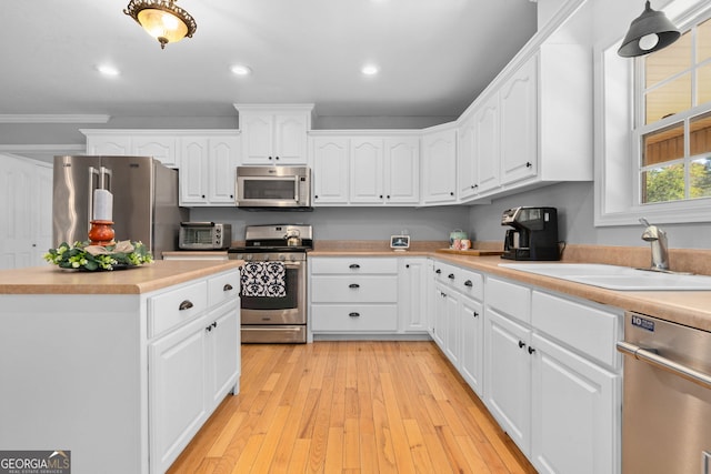 kitchen featuring light wood-type flooring, sink, crown molding, white cabinetry, and appliances with stainless steel finishes