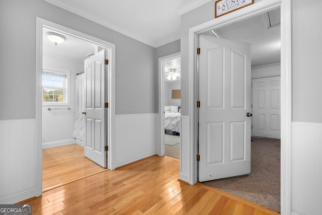 corridor with light wood-type flooring and crown molding