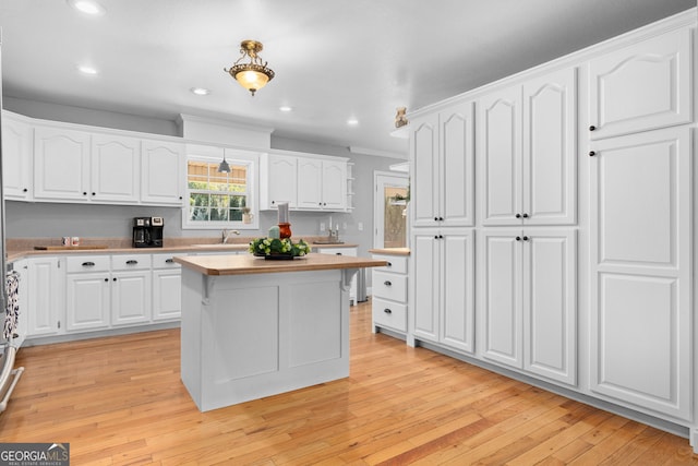 kitchen featuring pendant lighting, crown molding, light hardwood / wood-style flooring, sink, and white cabinets