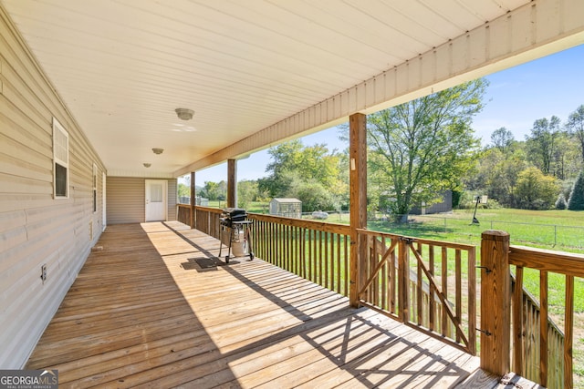 wooden terrace featuring a storage shed, a lawn, and a grill