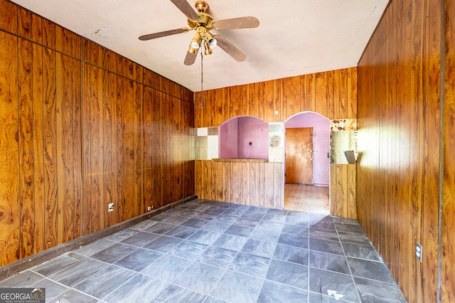 spare room with ceiling fan, a textured ceiling, and wood walls