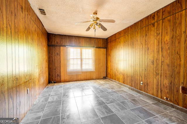 unfurnished room featuring wood walls, ceiling fan, and a textured ceiling