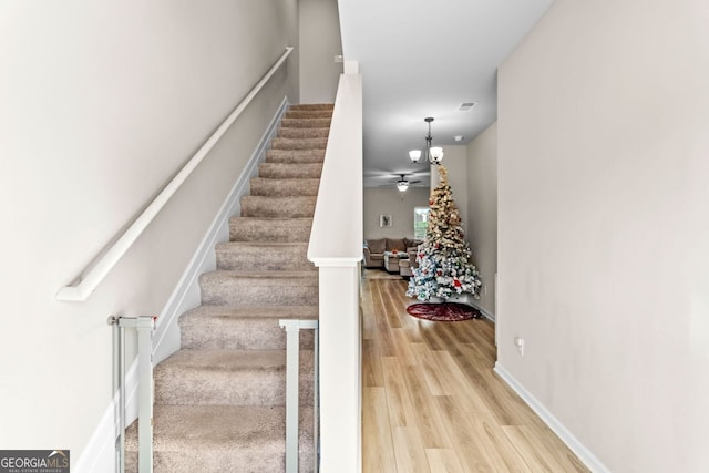 stairway with wood-type flooring and ceiling fan with notable chandelier