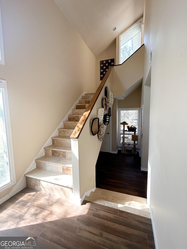 stairway with hardwood / wood-style flooring and high vaulted ceiling