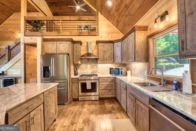 kitchen with lofted ceiling, wall chimney exhaust hood, wooden walls, sink, and appliances with stainless steel finishes