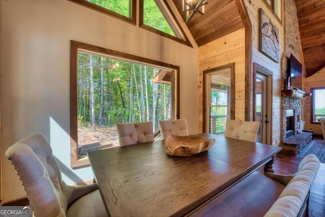 dining space with a stone fireplace, hardwood / wood-style floors, high vaulted ceiling, and wooden walls