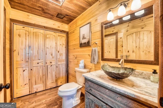 bathroom featuring hardwood / wood-style floors, wooden ceiling, toilet, vanity, and wooden walls