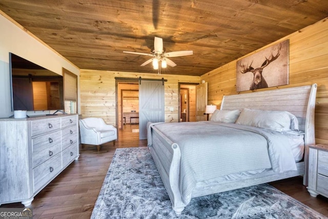 bedroom featuring dark hardwood / wood-style floors, a barn door, wooden walls, and ceiling fan