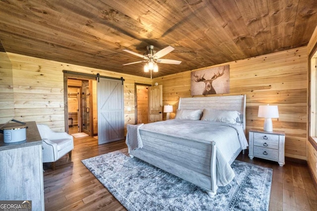 bedroom with wood walls, a barn door, ceiling fan, and dark hardwood / wood-style flooring