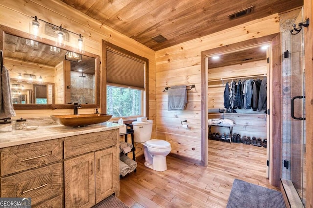 bathroom with hardwood / wood-style flooring, toilet, wood walls, vanity, and an enclosed shower