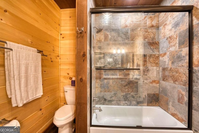 bathroom with toilet, wood walls, and combined bath / shower with glass door