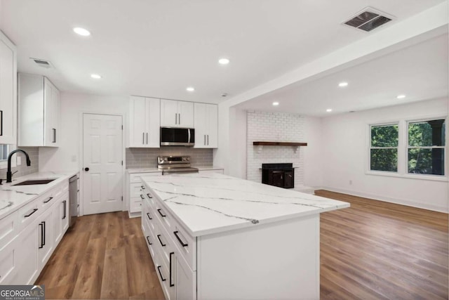 kitchen featuring white cabinets, appliances with stainless steel finishes, a kitchen island, sink, and tasteful backsplash