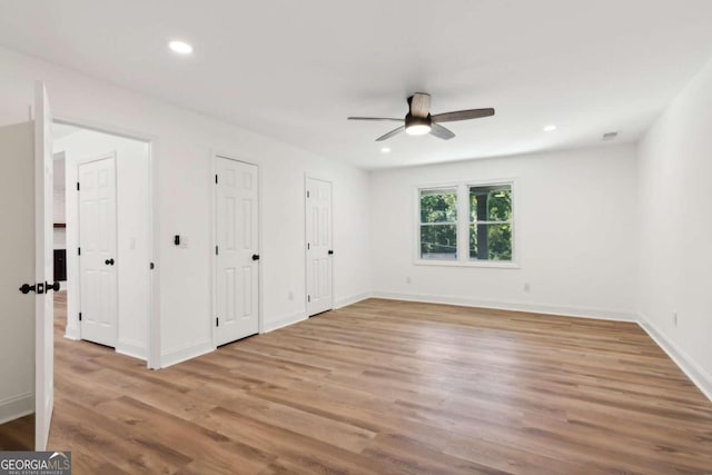 unfurnished bedroom featuring ceiling fan, light wood-type flooring, and two closets