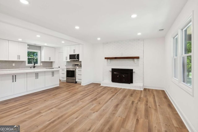 kitchen featuring white cabinetry, a fireplace, light hardwood / wood-style flooring, a healthy amount of sunlight, and appliances with stainless steel finishes