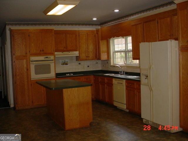 kitchen with white appliances, backsplash, a kitchen island, and sink