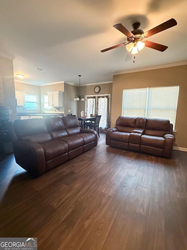 living room with ornamental molding, ceiling fan with notable chandelier, dark wood-type flooring, and a wealth of natural light