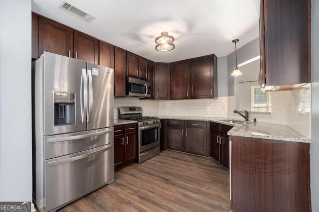 kitchen with hanging light fixtures, sink, appliances with stainless steel finishes, dark hardwood / wood-style floors, and light stone countertops