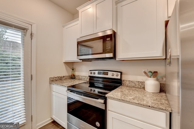 kitchen with stainless steel appliances, white cabinets, and light stone counters