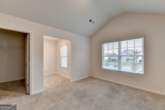 unfurnished bedroom featuring light colored carpet, vaulted ceiling, multiple windows, and a walk in closet