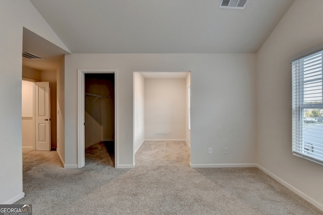 unfurnished bedroom with vaulted ceiling, a walk in closet, and light carpet