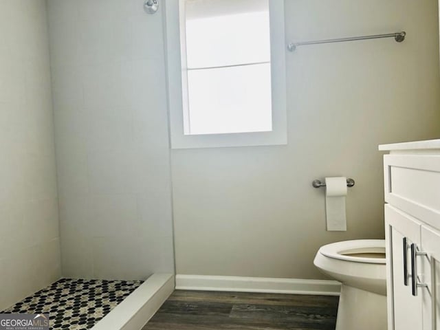 bathroom with wood-type flooring, a tile shower, vanity, and toilet