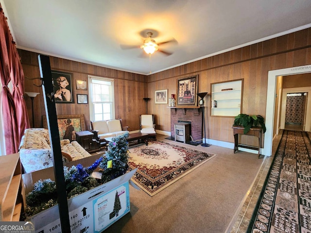 living room featuring wooden walls, ceiling fan, a wood stove, ornamental molding, and carpet