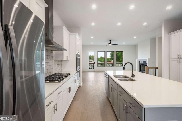 kitchen featuring white cabinets, a kitchen island with sink, wall chimney exhaust hood, appliances with stainless steel finishes, and light hardwood / wood-style floors