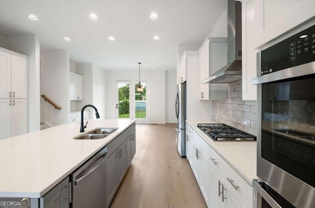 kitchen with wall chimney exhaust hood, sink, stainless steel appliances, hanging light fixtures, and white cabinetry