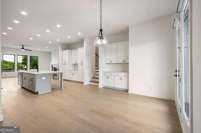 kitchen featuring an island with sink, decorative light fixtures, light hardwood / wood-style flooring, and white cabinetry