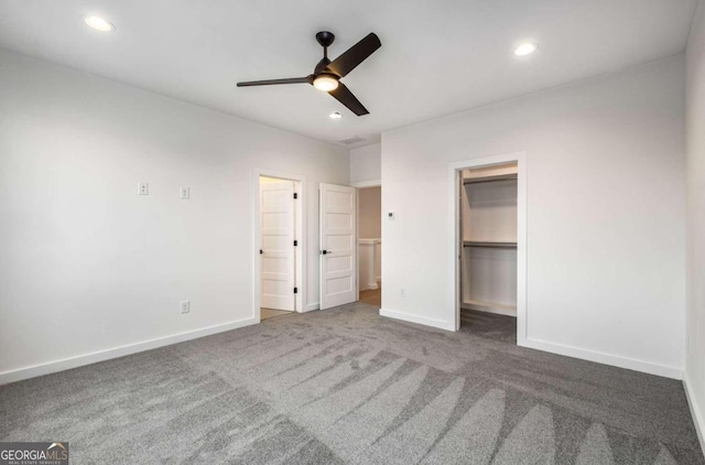 unfurnished bedroom with ceiling fan, a closet, dark carpet, and a walk in closet