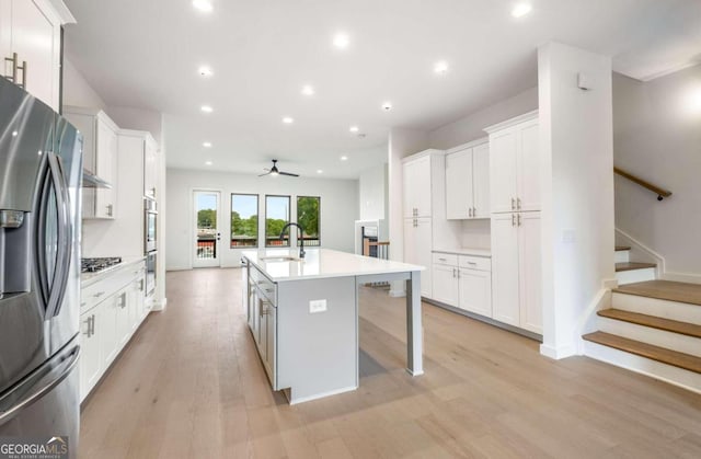 kitchen with light hardwood / wood-style flooring, a center island with sink, sink, stainless steel appliances, and white cabinets