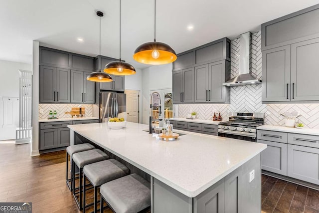 kitchen with wall chimney exhaust hood, a sink, appliances with stainless steel finishes, gray cabinetry, and decorative backsplash