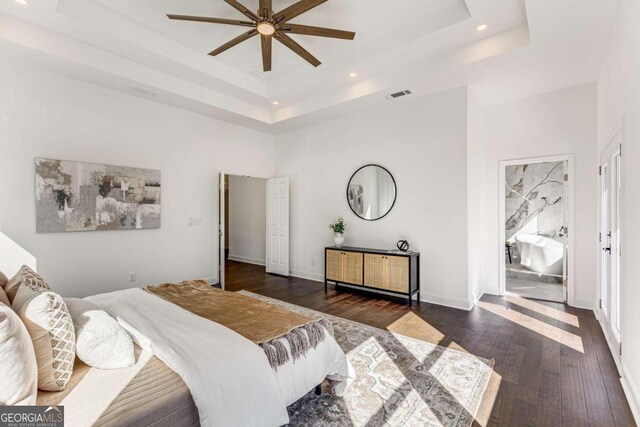 bedroom featuring dark hardwood / wood-style flooring, ceiling fan, connected bathroom, and a raised ceiling