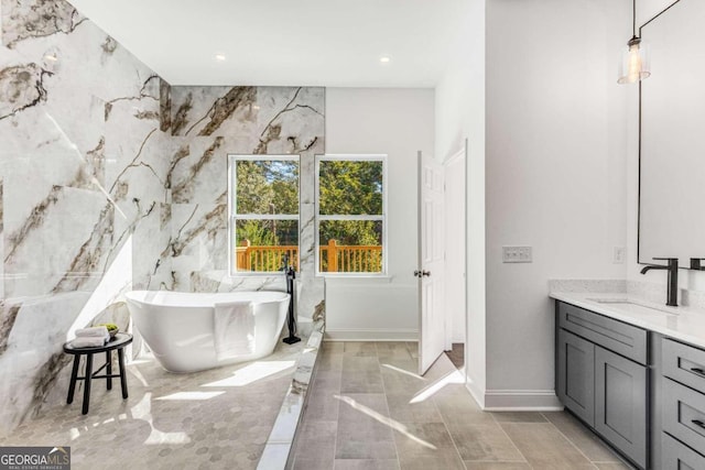 bathroom featuring baseboards, recessed lighting, a freestanding tub, and vanity