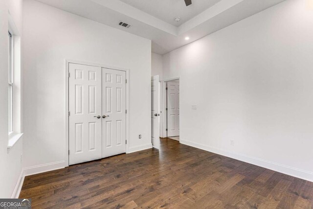 unfurnished bedroom with ceiling fan, a closet, dark hardwood / wood-style floors, and a towering ceiling