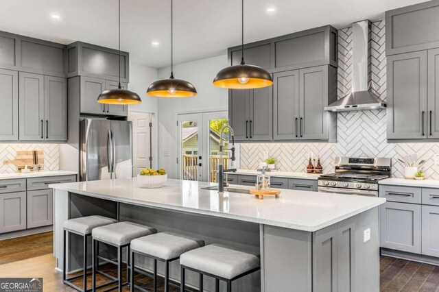 kitchen featuring wall chimney range hood, gray cabinets, decorative light fixtures, stainless steel appliances, and dark hardwood / wood-style floors