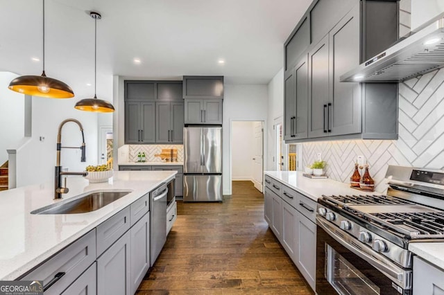 kitchen featuring wall chimney range hood, gray cabinets, appliances with stainless steel finishes, a sink, and backsplash