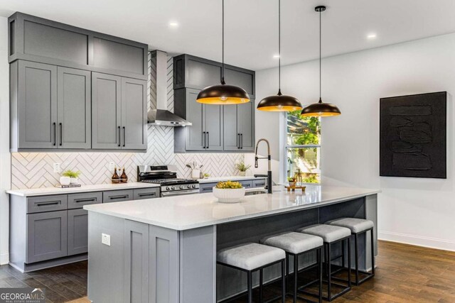 kitchen with hanging light fixtures, stainless steel gas range, dark hardwood / wood-style floors, and wall chimney range hood