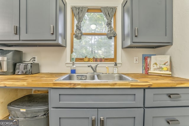 kitchen with wooden counters, a sink, and gray cabinetry