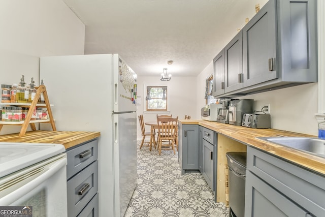 kitchen featuring pendant lighting, light floors, gray cabinets, wooden counters, and white appliances