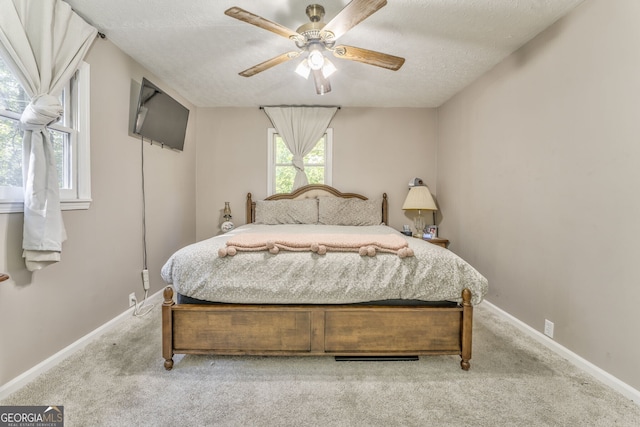 bedroom featuring light carpet, ceiling fan, baseboards, and a textured ceiling