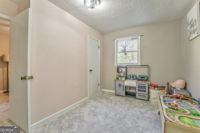 recreation room with baseboards, a textured ceiling, and light colored carpet