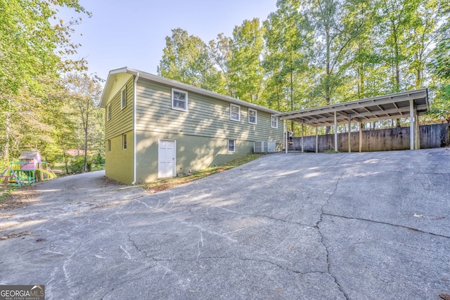 view of side of home featuring a carport, central AC, aphalt driveway, and a playground