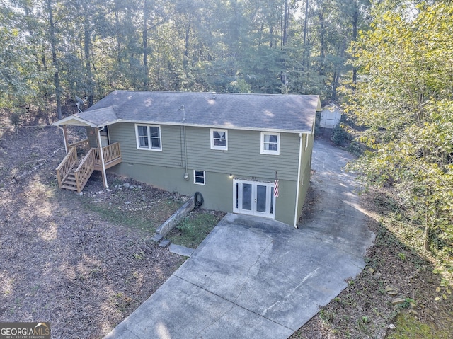 back of property with french doors, a shingled roof, concrete driveway, and stairs
