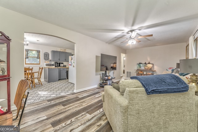 living room featuring dark wood-style floors, arched walkways, visible vents, ceiling fan, and baseboards