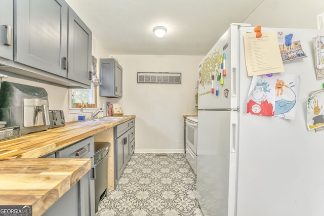 kitchen featuring butcher block counters, white appliances, a sink, baseboards, and gray cabinets