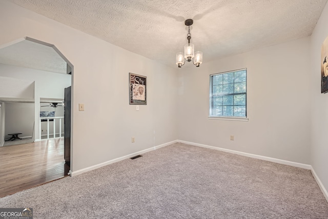 carpeted spare room with a textured ceiling and ceiling fan with notable chandelier