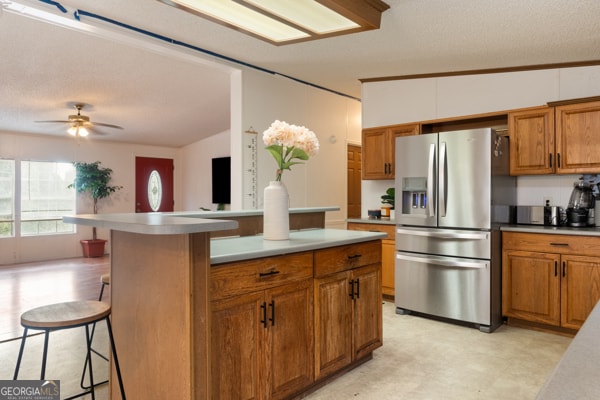 kitchen with lofted ceiling, ceiling fan, a kitchen breakfast bar, stainless steel fridge with ice dispenser, and a textured ceiling