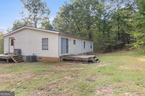 rear view of property featuring a yard, a deck, and central AC