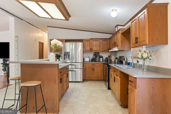 kitchen with appliances with stainless steel finishes, sink, a kitchen island, vaulted ceiling, and a breakfast bar